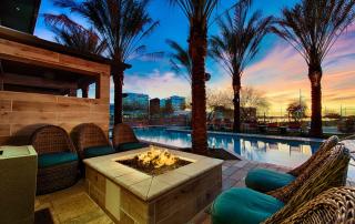 Tempe, AZ Luxury Apartments - Vela At Tempe Town Lake - Poolside Lounge Area With Raised Firepit, Outdoor Seating, Palm Trees, And City View