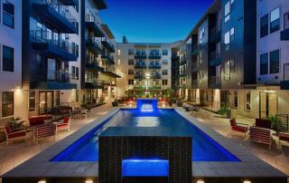 Pet-Friendly Luxury Apartments In Tempe, AZ - Vela At Tempe Town Lake - Sparkling Pool With Spa Cabanas, Waterfalls, Seating Area, And View Of Apartment Complex