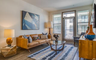 Apartments in Tempe AZ - Vela at Tempe Town Lake - Living Room with Large Windows, Couch, Chair, Area Rug, Coffee Table, and Floor Lamp.